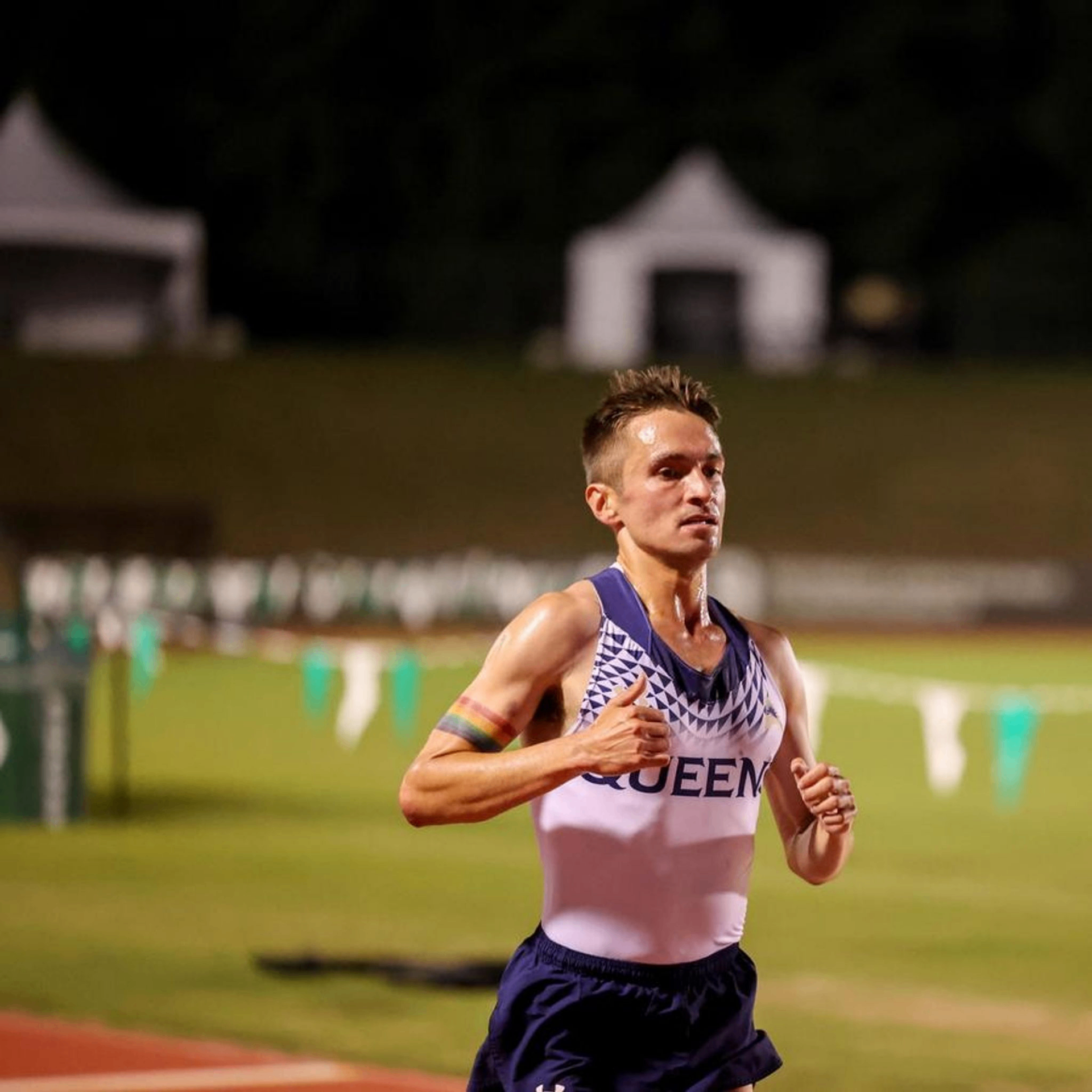 Lance racing for Queens University at night, wearing a Pride armband